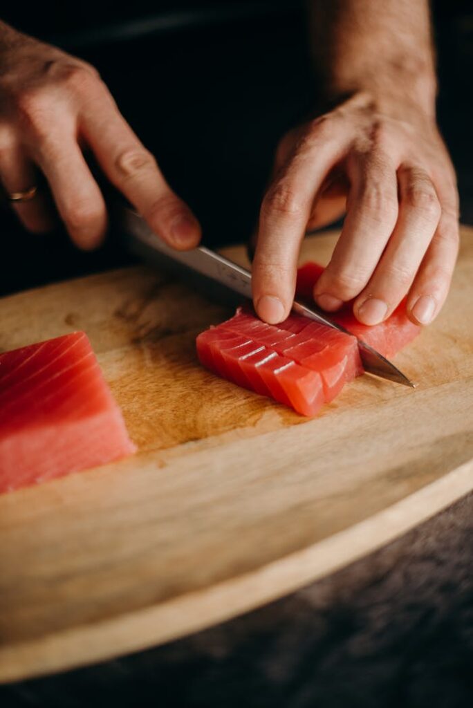 Close-up of hands slicing fresh tuna on a wooden cutting board, perfect for Asian cuisine themes.